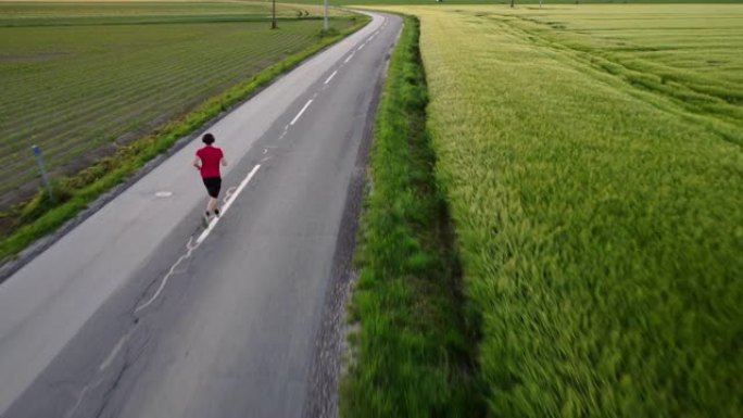 男运动员在被草地包围的高速公路上慢跑的鸟瞰图，跟踪户外追逐的镜头