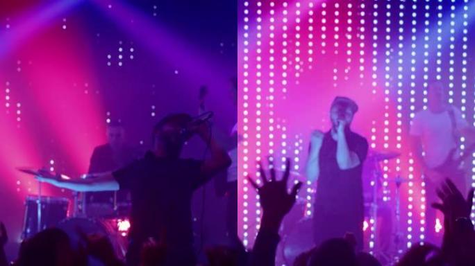 摇滚乐队在夜总会音乐会上表演的垂直镜头。前排人群正在聚会。歌迷的剪影在舞台上明亮的彩色频闪灯前举手。