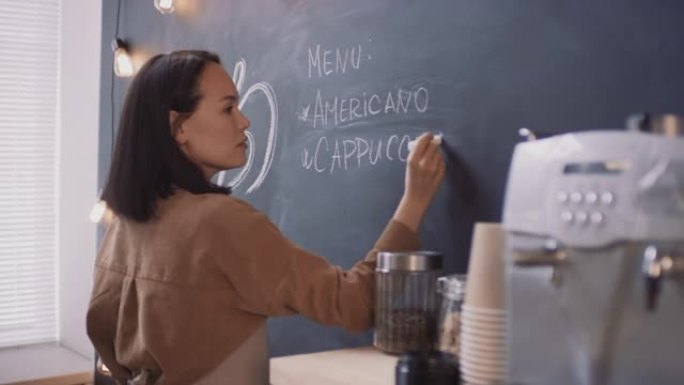 亚洲咖啡店工人在黑板上写作