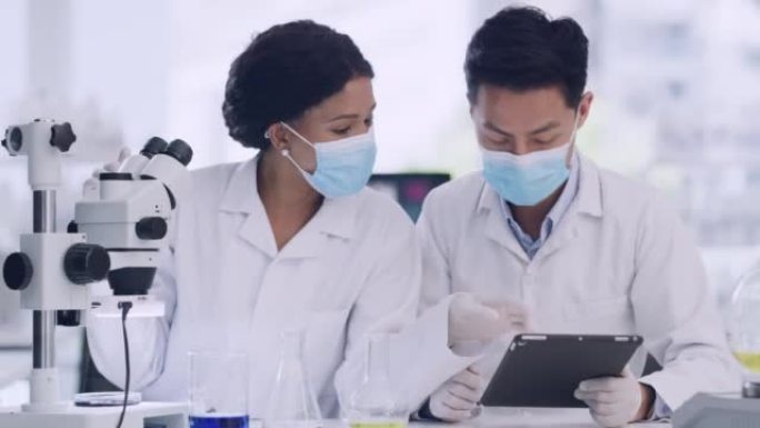 两名医学科学家在研究设施内使用平板和显微镜检查病毒样本。专家将数据输入系统，并对其进行分析，以实现突