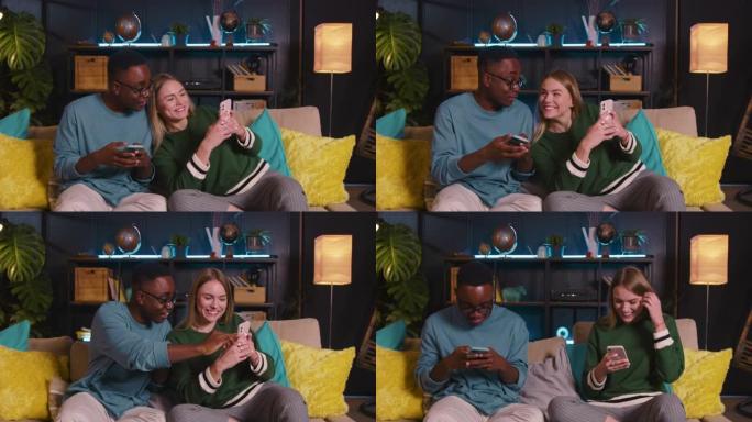 两个开朗的年轻快乐的多民族朋友使用手机在线购物，一起在家里的沙发上玩游戏。