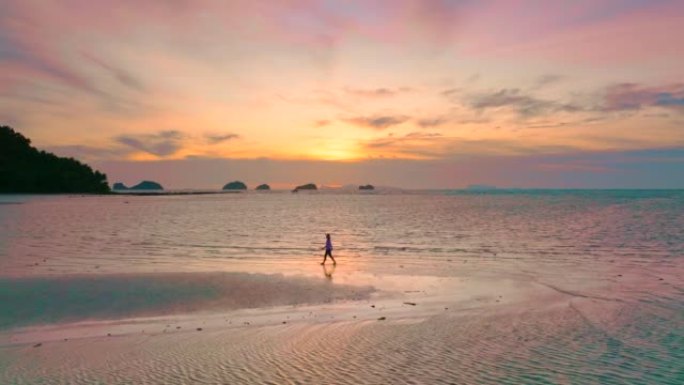 鸟瞰图日落时分，在沙滩上孤独行走的女人