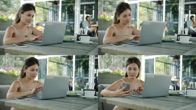 美丽的年轻女士在户外咖啡馆的餐桌上使用笔记本电脑和智能手机的肖像