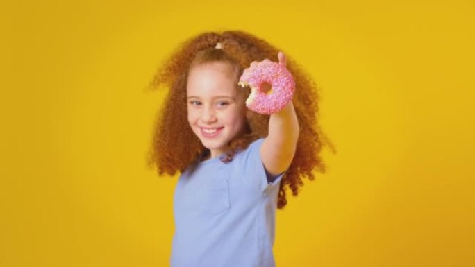 红头发女孩在黄色背景下吃甜甜圈的工作室镜头 -- 慢动作镜头