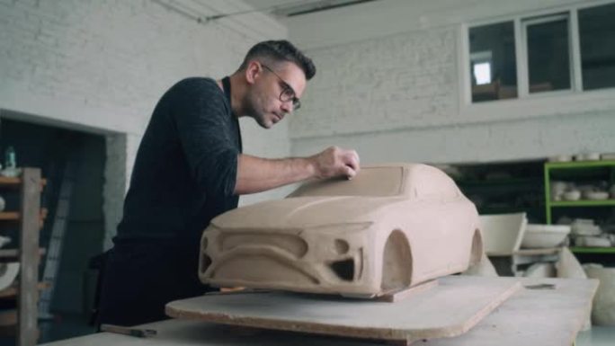 陶艺家在未完成的由粘土制成的汽车雕塑的设计细节上工作