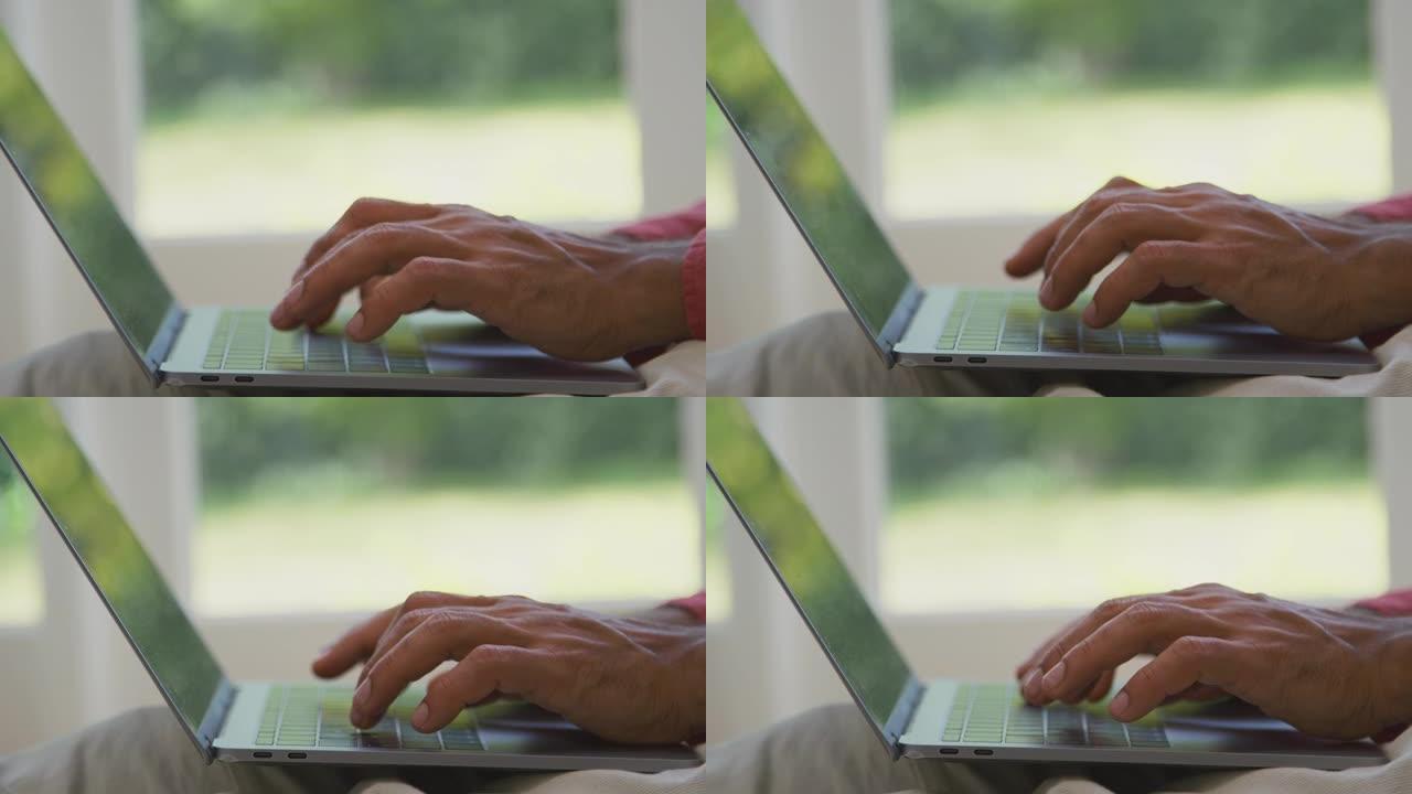 当男人在家坐在休息室的地板上工作时，手指在笔记本电脑键盘上的特写镜头