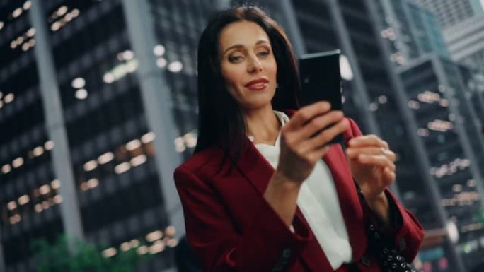 在大城市的街道上使用智能手机的成功成年女商人的肖像。自信的经理在去办公室的路上与网上的人联系，发信息