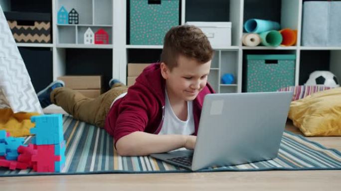 快乐的孩子在家里用笔记本电脑打字和微笑躺在地板上