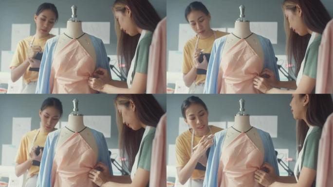 两位专业的亚洲开朗的女士时装设计师团队合作，用假人上的数字平板测量卷尺在商店里创造服装设计。女士裁缝