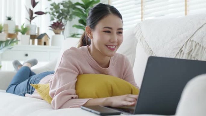 年轻的亚洲女性在家里沙发上使用电脑工作。