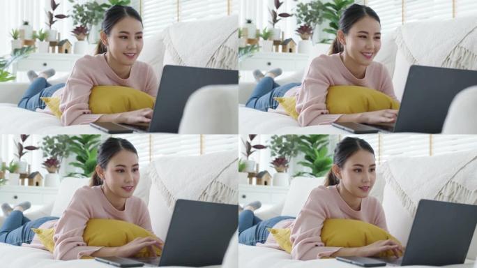 年轻的亚洲女性在家里沙发上使用电脑工作。