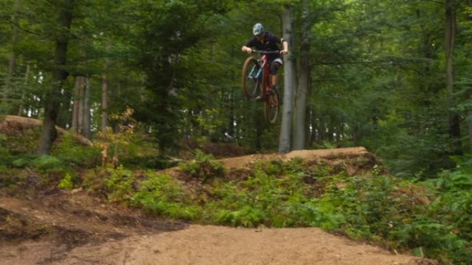 在绿色森林的泥泞小径上骑自行车，跳下悬崖