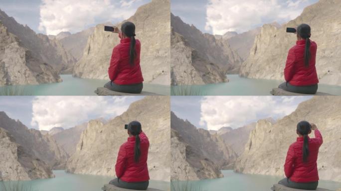 自由旅行者穿着红色冬装的年轻女性用智能手机拍摄美丽的景色，享受湖边的旅行假期。种族多样化的旅行者概念