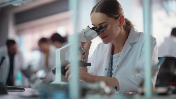 年轻的专业女工程师在实验室中使用显微镜检查电气组件的肖像。在一家工业制造公司担任实验室专家的成功女性