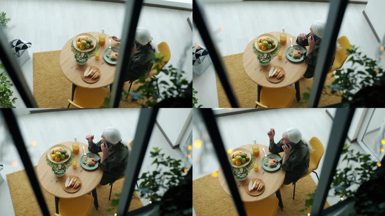 女士在手机上聊天，独自在现代公寓里吃午饭的俯视图