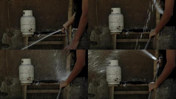 年轻女子在家中拿着水管给植物浇水，背景是家用煤气罐。特写。