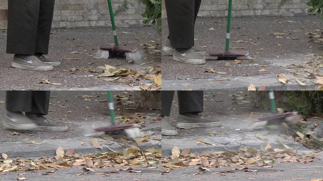 老人在街上用扫帚清理树叶。低角度视图。