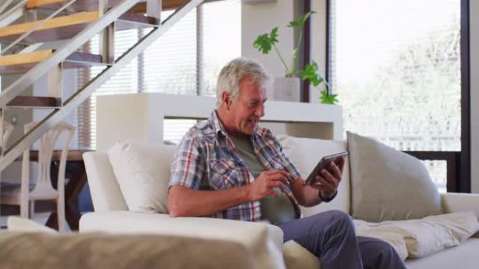 高个子白人坐在家里的沙发上在数字平板电脑上进行视频聊天