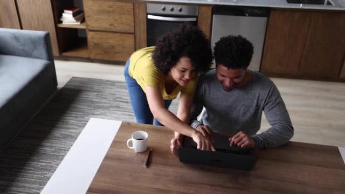 快乐的拉丁美洲夫妇在网上浏览时在家中使用笔记本电脑