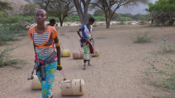 气候变化。干旱。水危机。特写正面视图。由于持续干旱，非洲妇女用塑料容器走路和滚动回家。肯尼亚