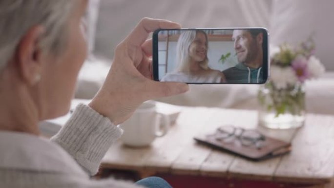 成熟的女人使用智能手机与幸福的夫妇聊天，在手机屏幕上与祖母分享激动人心的订婚，享受家庭联系4k