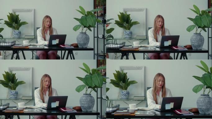放大美丽严肃成功的金发老板商界女性在现代轻便的办公桌上用笔记本电脑独自工作。