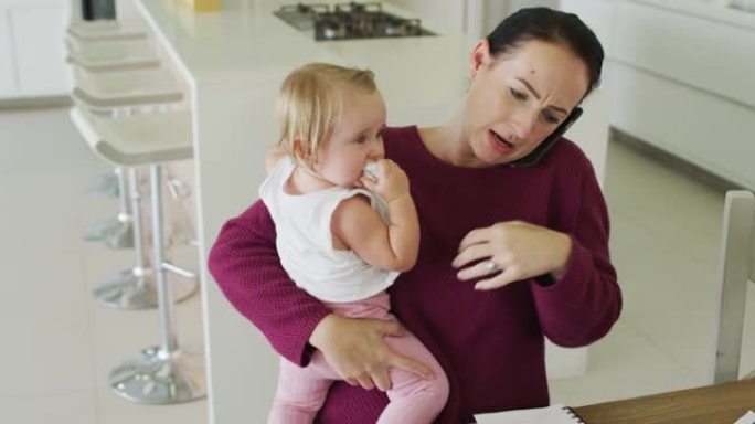 高加索母亲抱着婴儿并在家中使用智能手机聊天