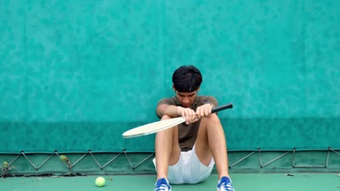 失望的男子网球运动员坐在球场上。