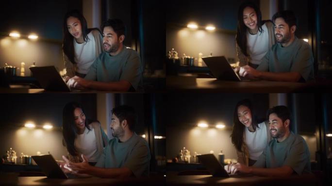 年轻夫妇坐在家里的厨房里使用笔记本电脑的肖像。快乐兴奋的女人帮助她的伴侣解决与工作相关的问题，为他提
