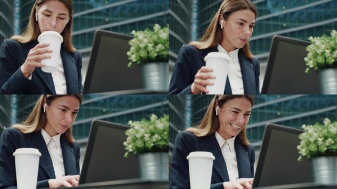 在摩天大楼背景下，在办公室附近的酒吧里喝早间咖啡时，女商人使用笔记本电脑工作的电影镜头。技术、网络、