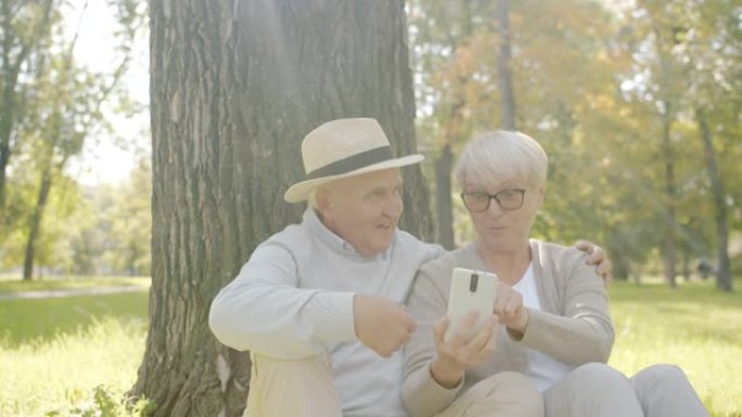 快乐的高级夫妇在阳光明媚的日子里看着智能手机屏幕在公园玩得开心