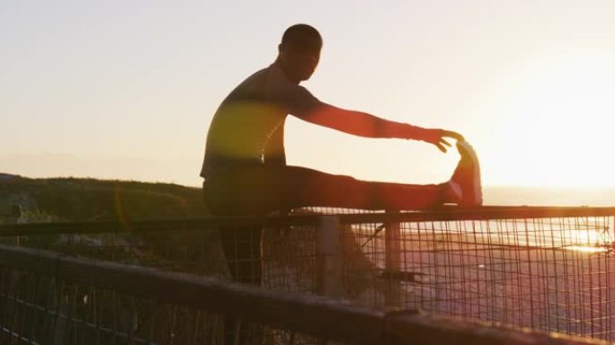 专注的非洲裔美国男子伸展运动，在日落时在海边户外运动