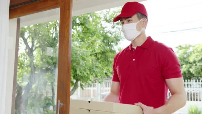 年轻的邮政快递快递员戴着口罩处理食品盒，在家里寄给顾客，亚洲男性在户外接收快递包裹。