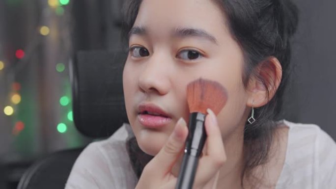 年轻的亚洲有影响力的女孩vloging演示如何用美容化妆品化妆。她在家里的客厅里用相机记录在线辅导班