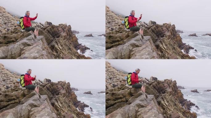 徒步旅行时，背包坐在岩石上并在智能手机上拍照的高级徒步旅行者