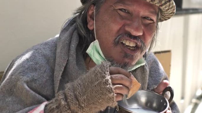 在covid-19冠状病毒大流行期间，戴着外科口罩乞讨的无家可归者正在吃食物