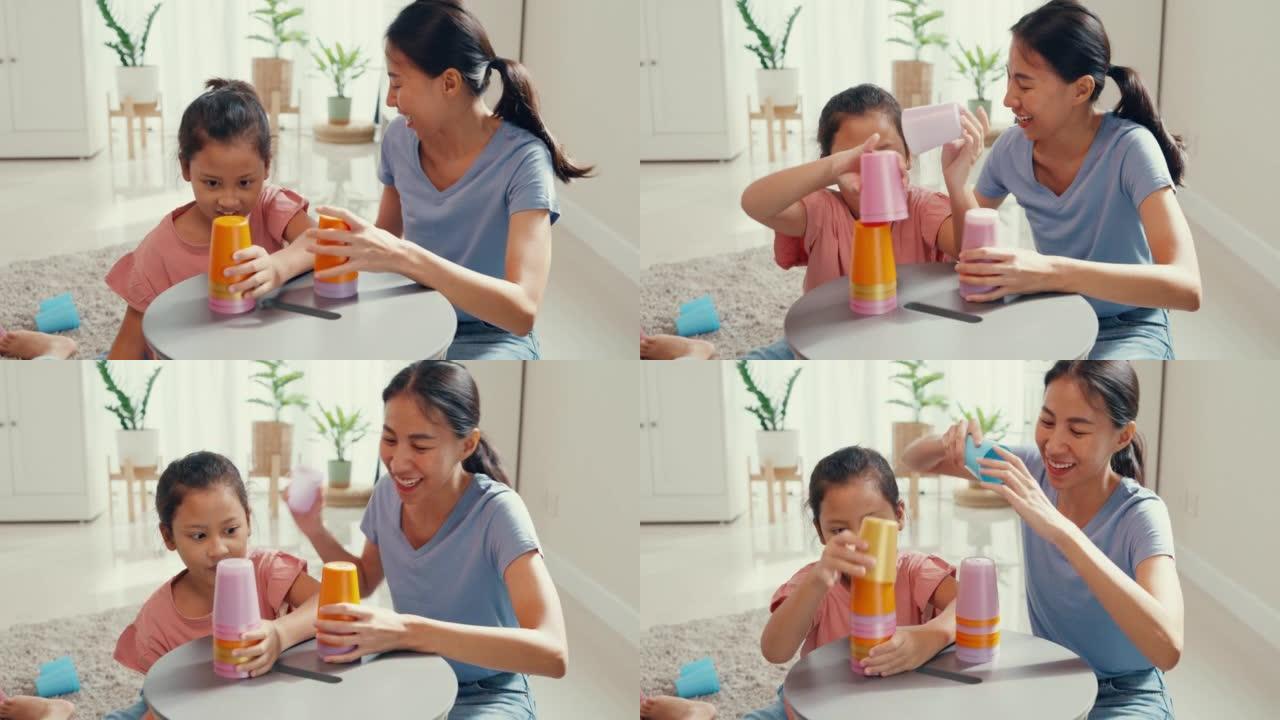 亚洲蹒跚学步的小女孩和妈妈坐在地毯上，开心的时刻在家里客厅的桌子上玩彩色堆栈杯玩具。