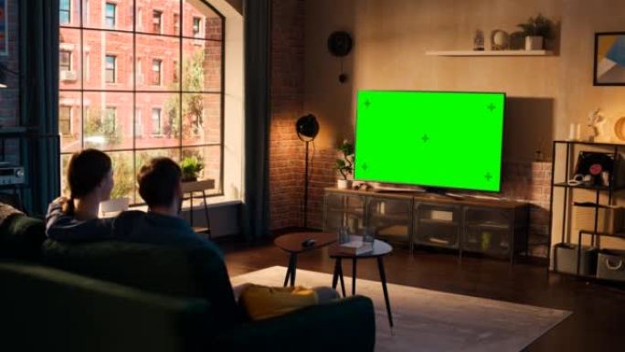 真正的情侣在家里度过时光，坐在沙发上，在他们时尚的阁楼公寓里看绿屏模拟显示的电视。男人和女人流媒体电