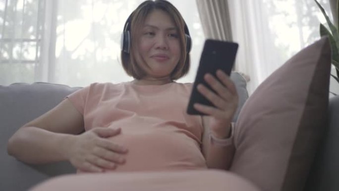 亚洲孕妇在家放松时用耳机听音乐