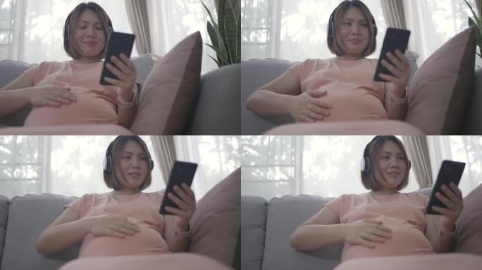 亚洲孕妇在家放松时用耳机听音乐