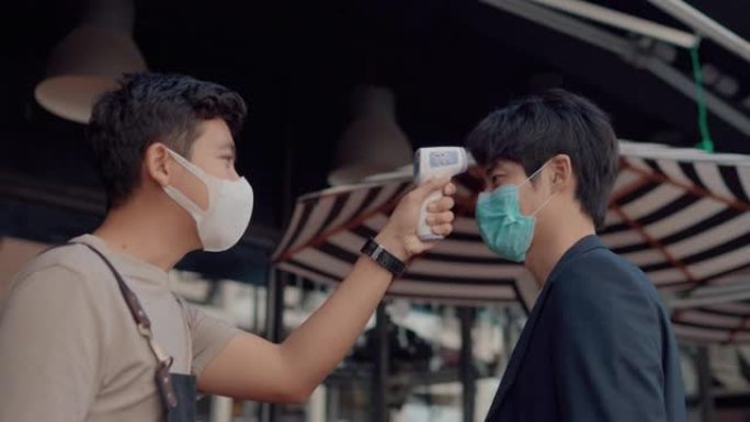亚洲咖啡店的工作人员戴着外科口罩，在商店入口处为顾客做温度检查。