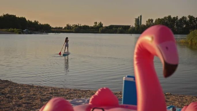 SLO MO Flamingo游泳浮标vs女子站立划桨在湖上
