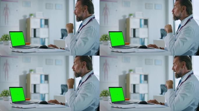 家庭医生正在健康诊所的绿屏显示的计算机上与患者进行视频通话。穿着实验室外套的助理正在医院办公室谈论健