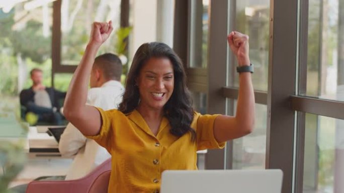 兴奋的成熟女商人用笔记本电脑庆祝好消息在办公室的办公桌上工作