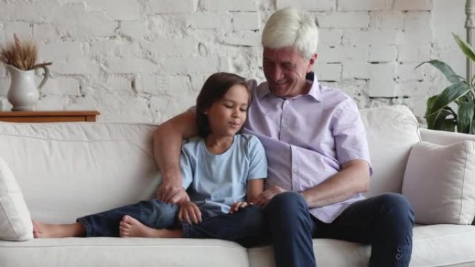 慈爱的祖父拥抱他的孙子聊天坐在沙发上