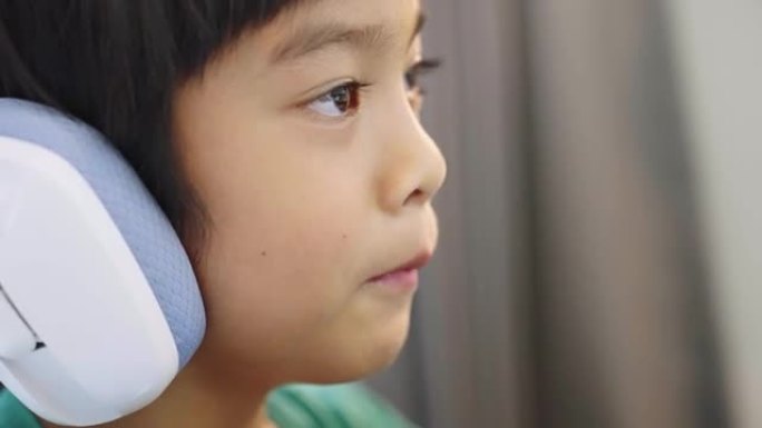 亚洲小男孩戴着耳机说话，在家在台式电脑上在线玩视频游戏。