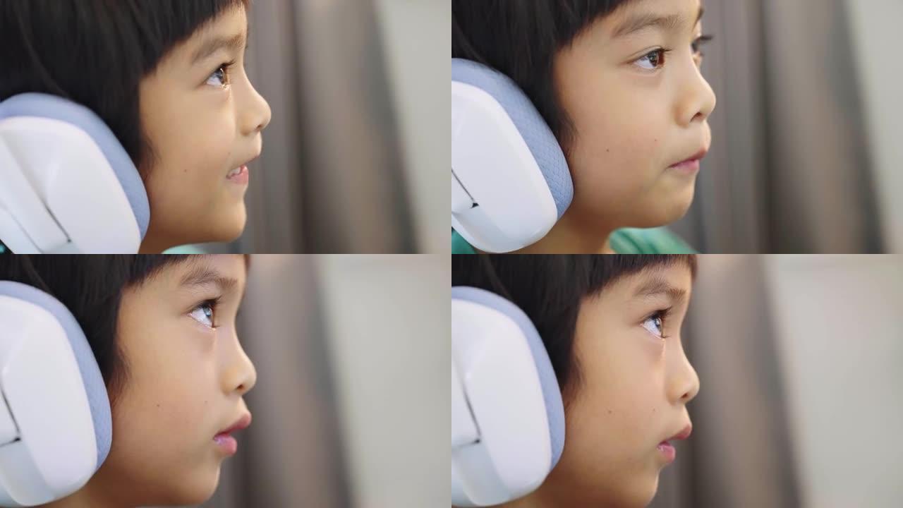 亚洲小男孩戴着耳机说话，在家在台式电脑上在线玩视频游戏。