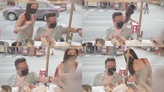 亚洲中国男性残疾人坐在轮椅上的女性朋友在八打灵街选择食物享受街头美食