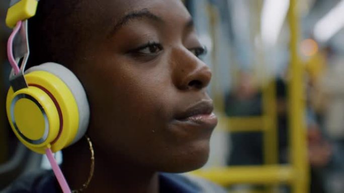 微笑的黑人妇女在乘火车旅行时戴上彩色耳机并收听播客的肖像。大学生在保持联系的同时享受在公共交通工具上