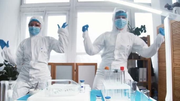 庆祝成功。两个兴奋的疯狂快乐的女性化学实验室医生穿着白色防护服在工作中做有趣的舞蹈。